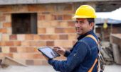 A building contractor wearing a hard hat and holding a tablet reviewing WEXCARD data at a jobsite.