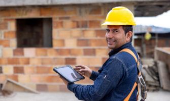 A building contractor wearing a hard hat and holding a tablet reviewing WEXCARD data at a jobsite.